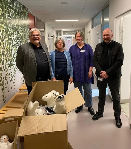 Fire personer står bag kasser med hvide bamser, der overdrages som donation
